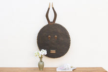 Decorative wall art with round face on a wooden surface against a white wall.
