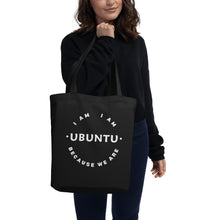 Person holding a black tote bag with 'I AM I AM UBUNTU BECAUSE WE ARE' text.