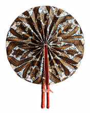 A round folding hand fan with a brown, gold, and white batik-style geometric and floral pattern, featuring two red wooden handles secured by a leather strap, shown against a plain white background.