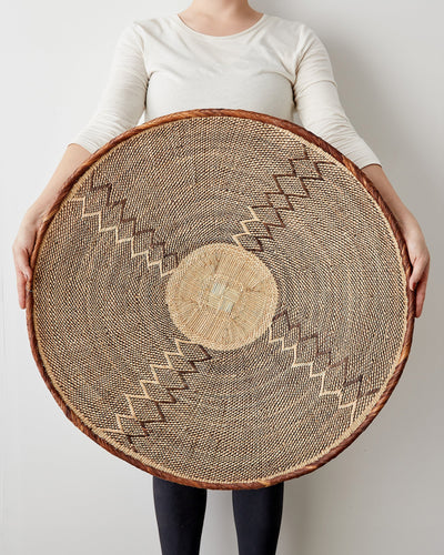 Person holding a large woven basket with geometric patterns on a plain background