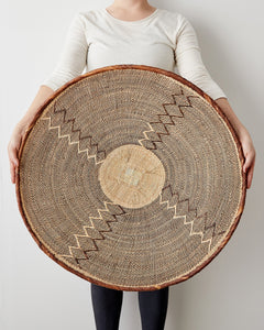 Person holding a large woven basket with geometric patterns on a plain background