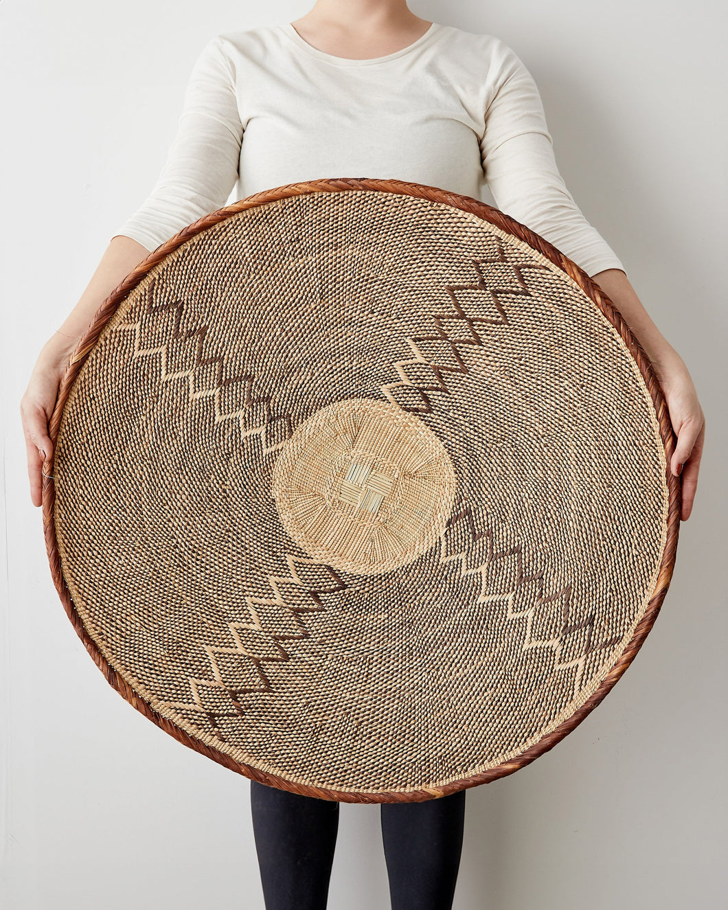 Person holding a large woven basket with geometric patterns on a plain background