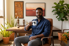 Man sitting in a chair holding a mug in a room with plants and artwork.