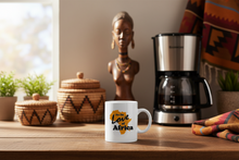 White mug with 'For the Love of Africa' text on a wooden table with a coffee maker and decorative items.