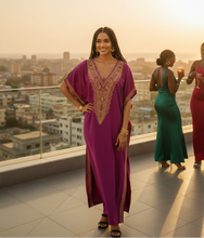 Woman in a purple dress with gold embroidery standing on a rooftop with a cityscape in the background.