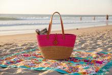 Pink and brown tote bag on a colorful beach towel with a beach background