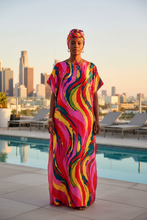 Woman in a colorful kaftan dress standing by a pool with a city skyline in the background