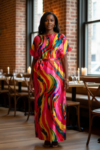 Woman in a colorful kaftan dress standing in a restaurant with brick walls and large windows.