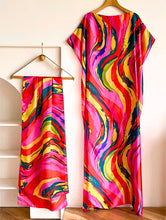 Colorful kaftan dress with a matching scarf on hangers against a neutral background