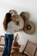 Woman arranging woven baskets on a wall in a home setting