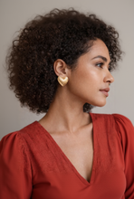 Woman wearing gold heart-shaped earrings with a neutral background