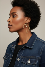 Woman wearing a denim jacket and Africa-shaped earrings on a neutral background