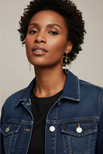 Woman wearing a denim jacket and African earrings with a neutral background