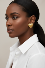 Woman wearing gold heart-shaped earrings with a neutral background