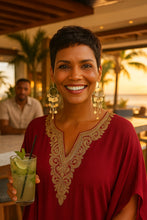 Woman in a red dress wearing long tassel earrings holding a cocktail with a sunset background