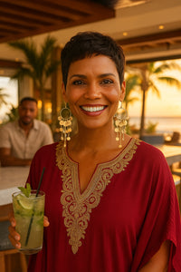 Woman in a red dress wearing long tassel earrings holding a cocktail with a sunset background