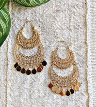 Gold African inspired earrings with black and red stones on a textured fabric background
