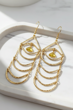Long gold tone earrings on a marble jewelry tray.