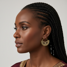 Woman wearing gold earrings and a maroon top with gold trim against a neutral background