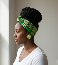 Woman wearing a green and black patterned headscarf and earrings against a neutral background