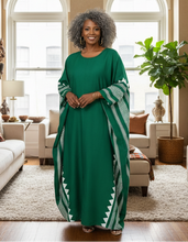 Woman in a green dress standing in a living room with large windows and decor.