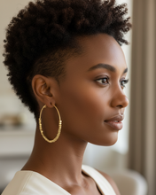Gold hoop earrings with beaded design worn by a person against a neutral background