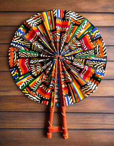 Colorful kente cloth patterned fan with leather handle on a wood background