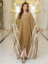 Woman wearing a long, light brown dress with white patterns in an elegant indoor setting.