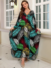 Woman wearing a colorful leaf-patterned dress indoors.