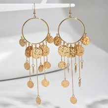 Gold hoop earrings with dangling coins and chains on a white background
