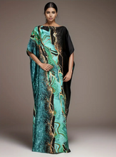 Woman wearing a long, patterned dress with a gradient of green, black, and gold on a neutral background.