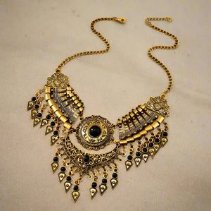 Decorative gold necklace with black accents on a wooden surface