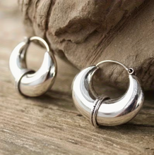 Silver hoop earrings on a wooden surface with a stone background