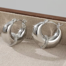 Silver hoop earrings on a textured surface with a wooden border.