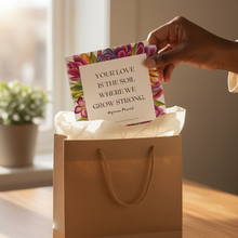 Hand placing a card into a gift bag with a floral design and text.
