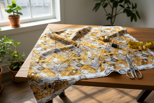 Fabric with a yellow and black pattern on a wooden table near a window with plants.