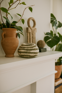 Decorative setup with a terracotta vase, striped wool basket, and plants on a white mantle.