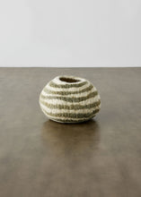 Small striped wool bowl on a reflective surface with a neutral background