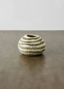 Small striped wool bowl on a reflective surface with a neutral background