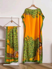 orange and green kaftan dress with peacock design with matching scarf on a wooden hanger against a white wall.