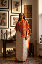 Woman in an orange kaftan dress standing in a room with framed artwork and sculptures.