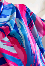 A close-up of a vibrant abstract print kaftan dress with swirling patterns of hot pink, bright blue, and light blue, draped elegantly.