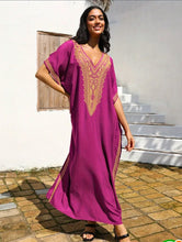Woman wearing a purple dress with gold embroidery standing outdoors.