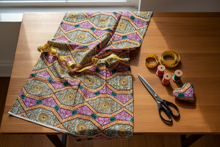Colorful African patterned fabric on a wooden table with scissors and spools of thread.