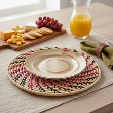 Table setting with a plate on a woven placemat, surrounded by fruits, cheese, and juice.