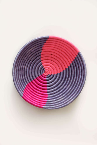 Round woven basket with pink and purple pattern on a white background