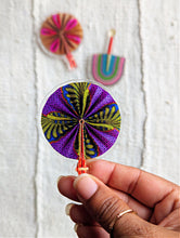 Purple African fabric hand fan magnet held by a hand against a light background