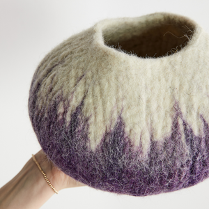 Textured wool vase with gradient color from beige to purple held by a person on a white background