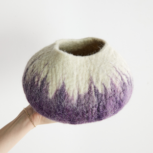 Handmade felted wool bowl with gradient color from white to purple held by a person on a light background