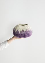 Hand holding a textured wool vase with a gradient from purple to beige on a light gray background